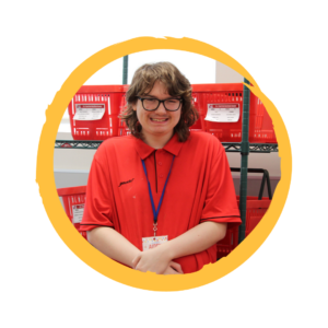 Aiden stands in front of red shopping baskets, wearing a red Schnucks polo and smiling.