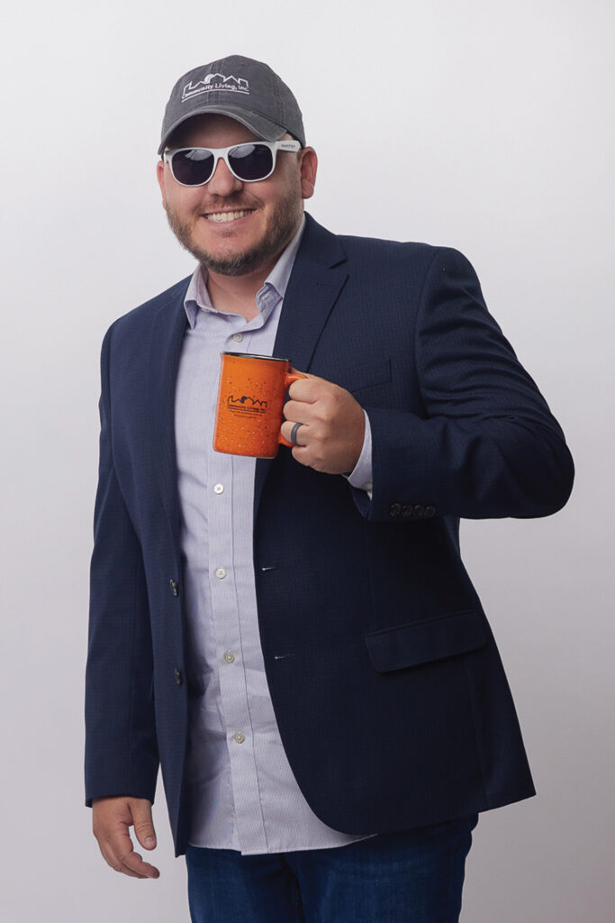 Dave wearing a baseball cap and sunglasses and holding an orange mug with a Community Living logo