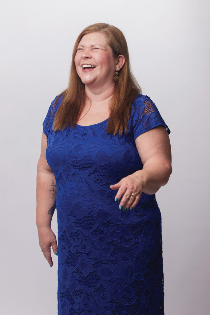Heather Bell wearing a blue dress and looking slightly off camera, laughing