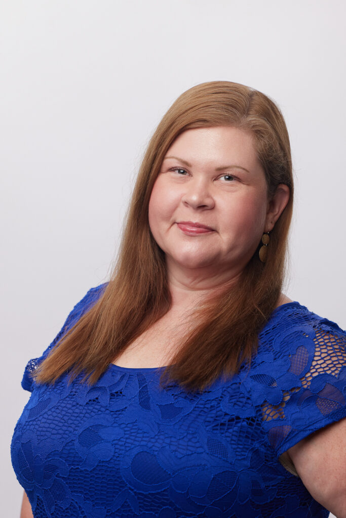 Heather Bell wearing a blue dress and smiling against a blank background