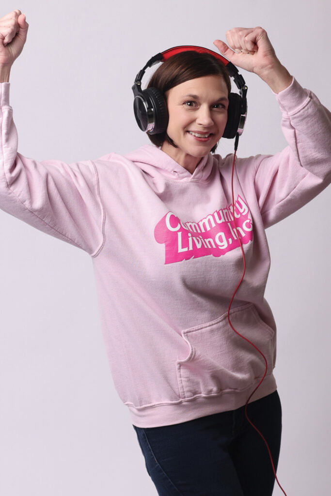 Jenn Braden wearing a pink hoodie and headphones while dancing with her arms in the air