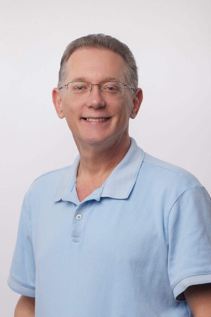 John Ditch wearing a light blue polo shirt and smiling against a blank background