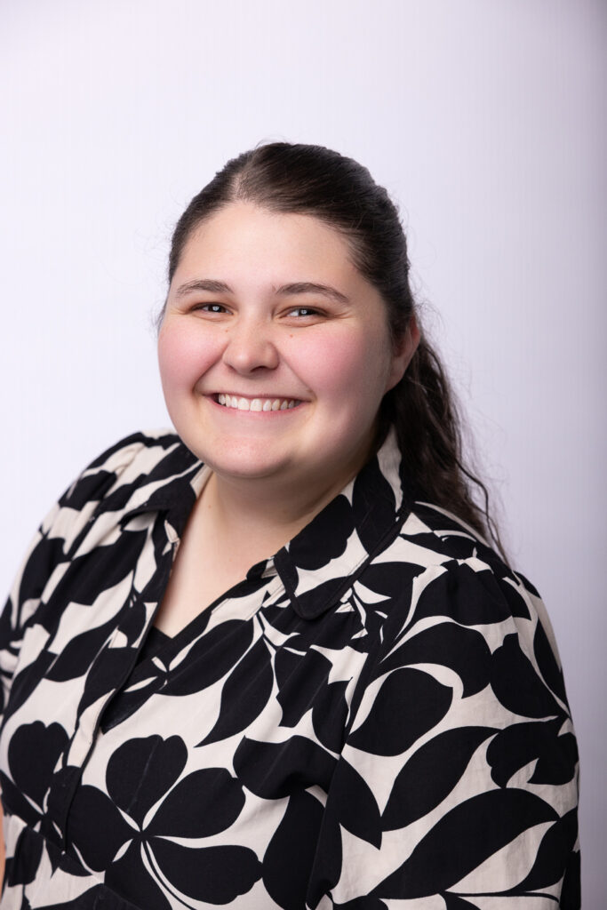 Hannah Dyer's headshot - wearing a black and tan floral pattern dress.