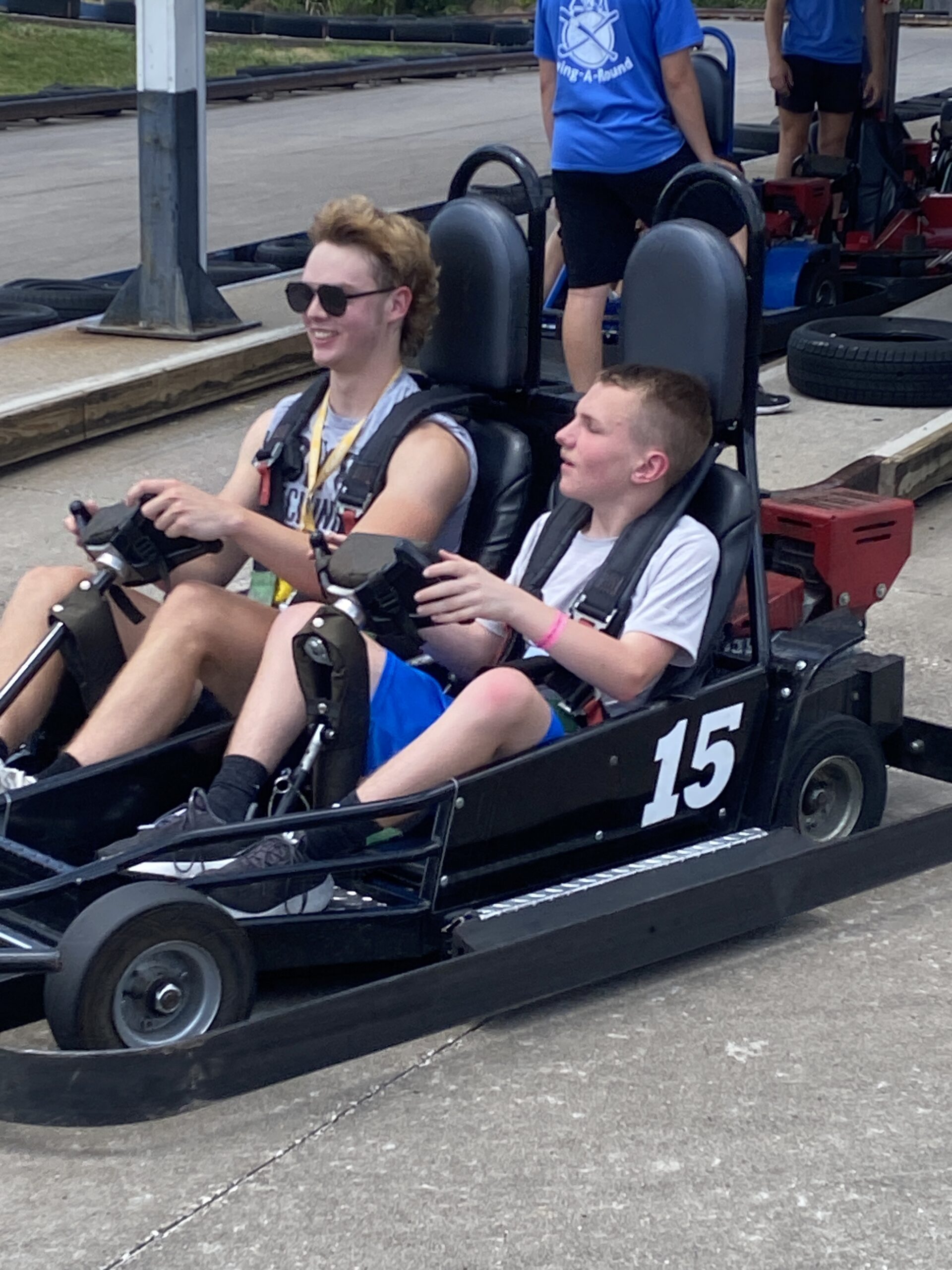 Alex and Support Staff drive a go-kart together, smiling.