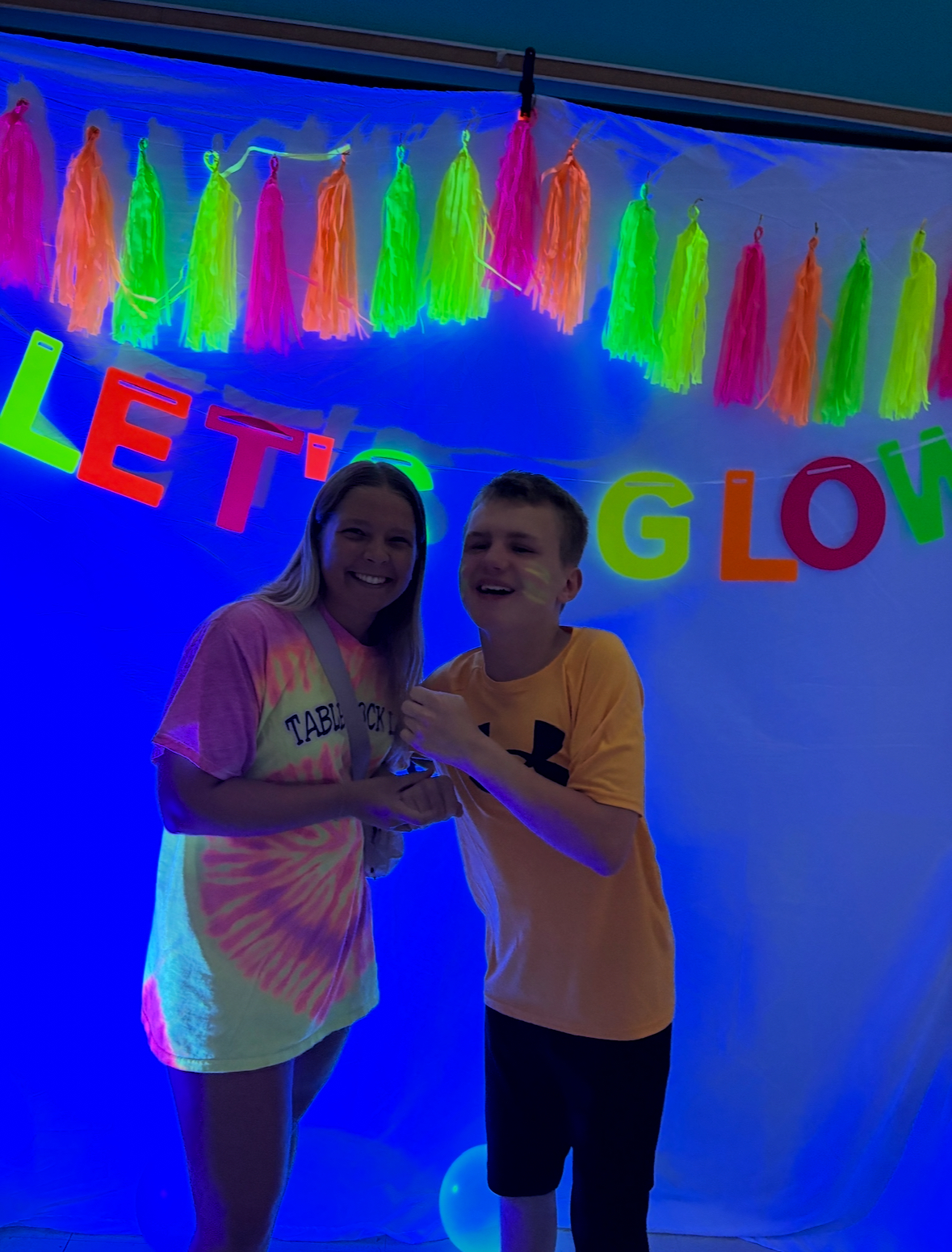 Alex smiling with support staff at a Teen Club black light party with neon decorations.