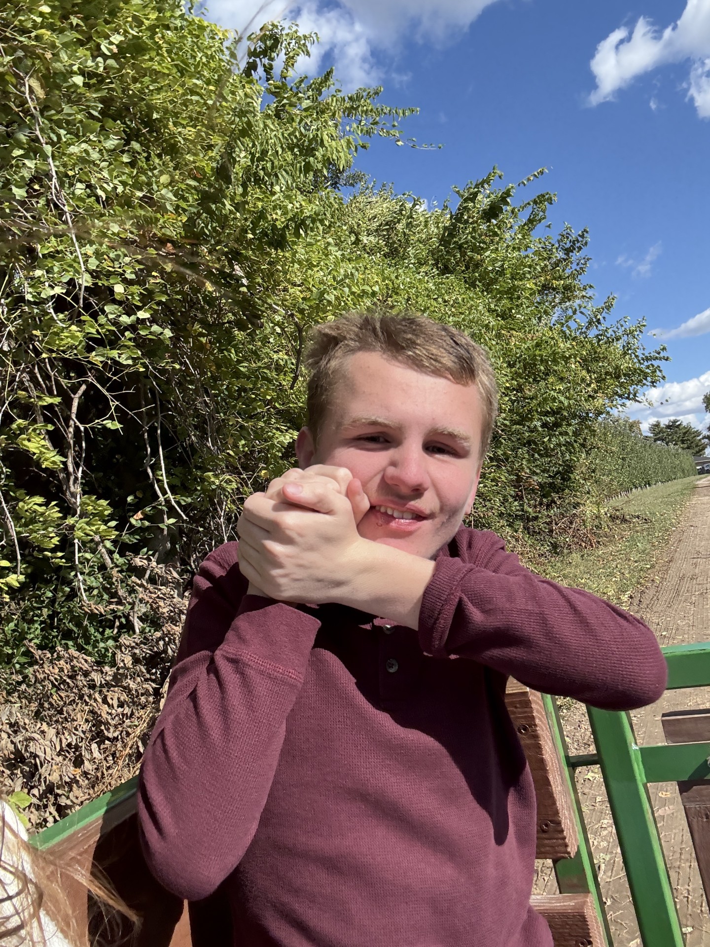 Alex smiles on a tractor wagon ride, with trees and blue skies behind him.