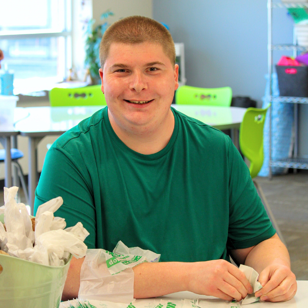 Participant sitting at table and smiling while working on a project using plastic bags.
