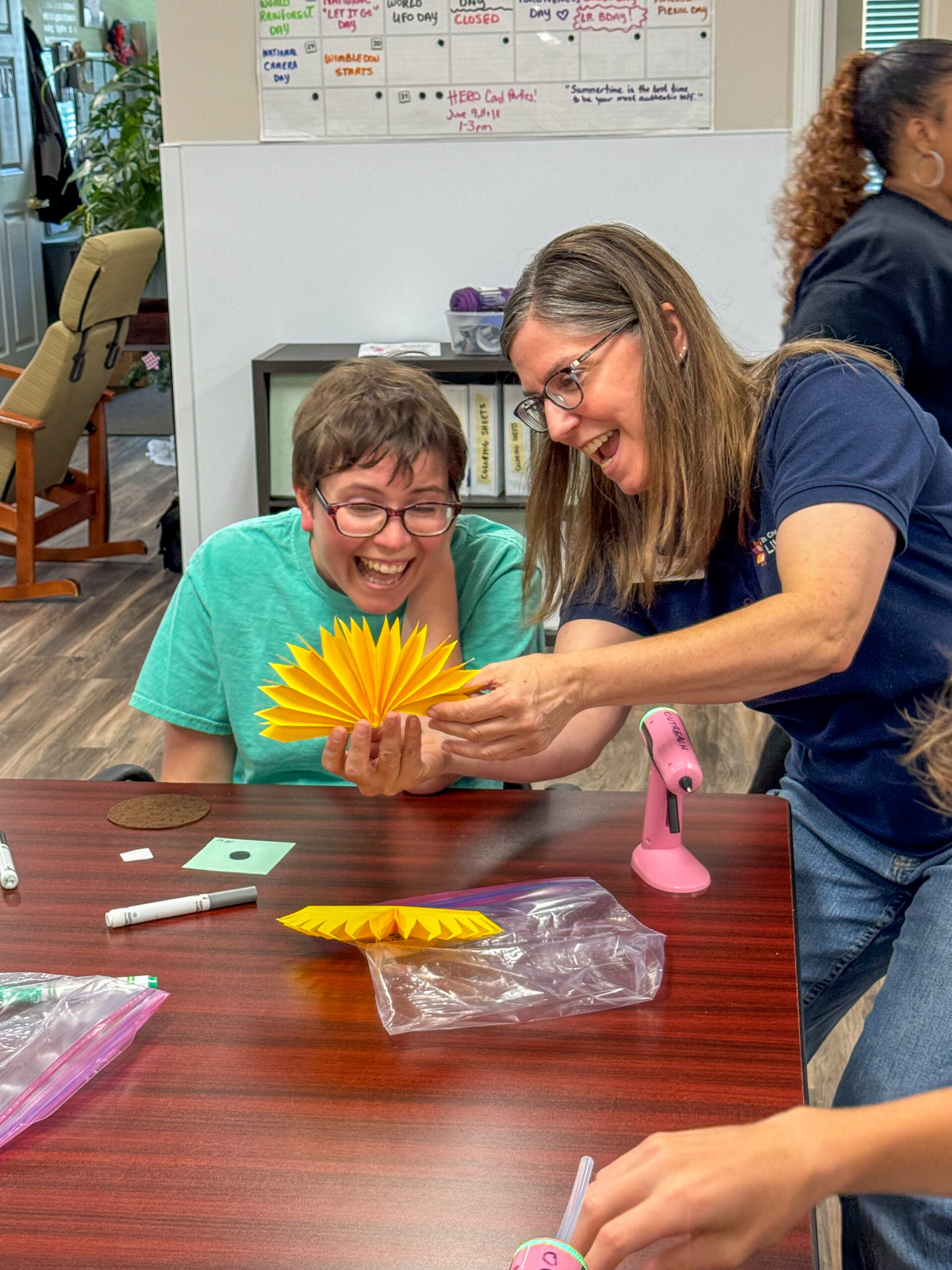 Allison and staff from local library smile as they craft a sunflower together with paper
