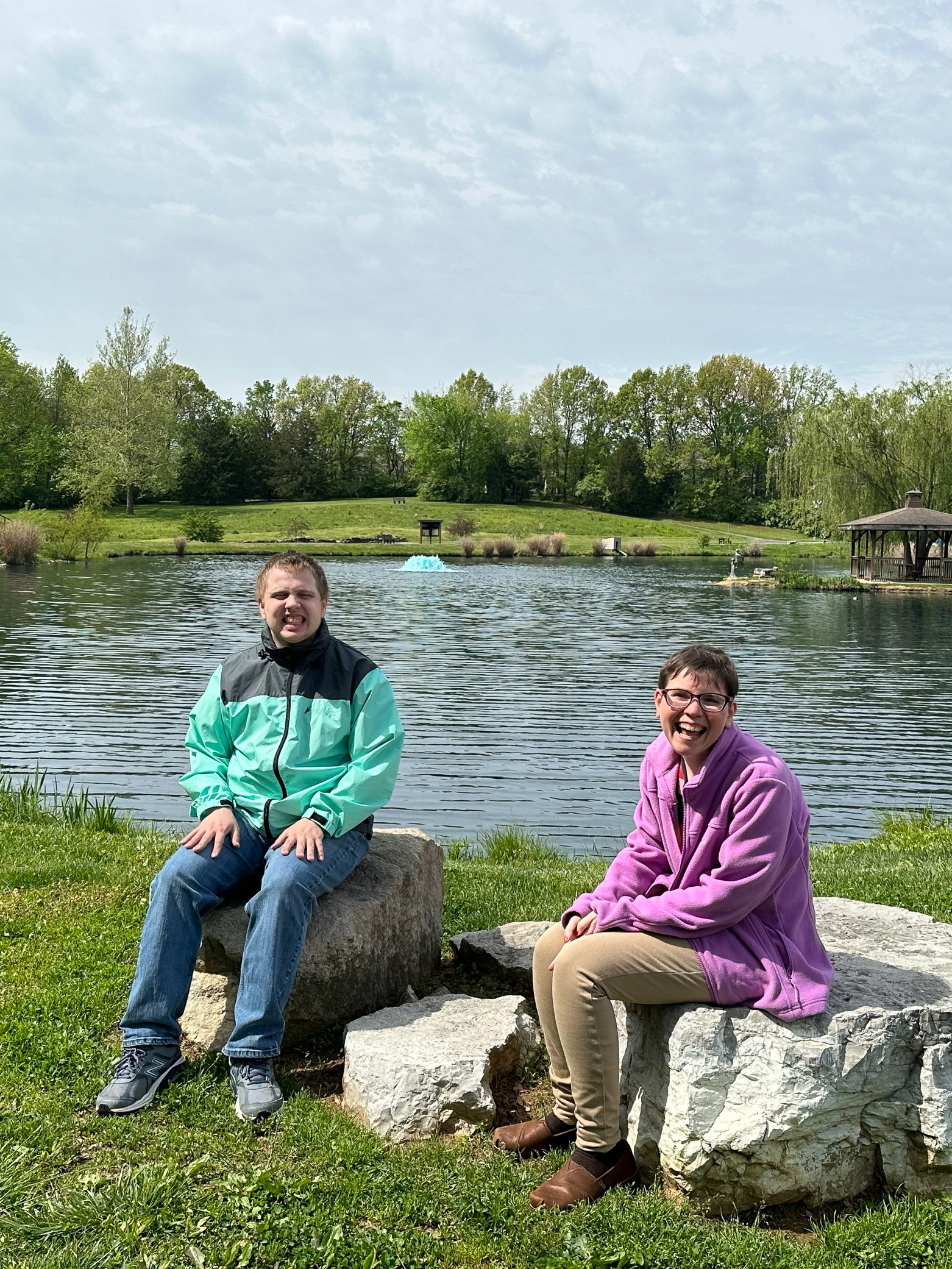 Allison and Mahon Center participant sit on big boulders at a park, in front of a pond.