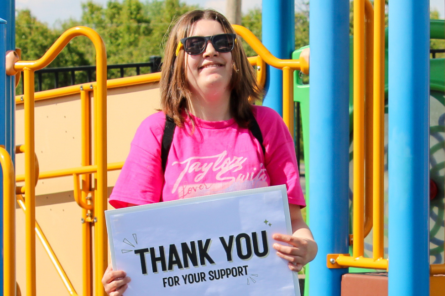 Girl holding a sign that says "thank you" while standing on a playground