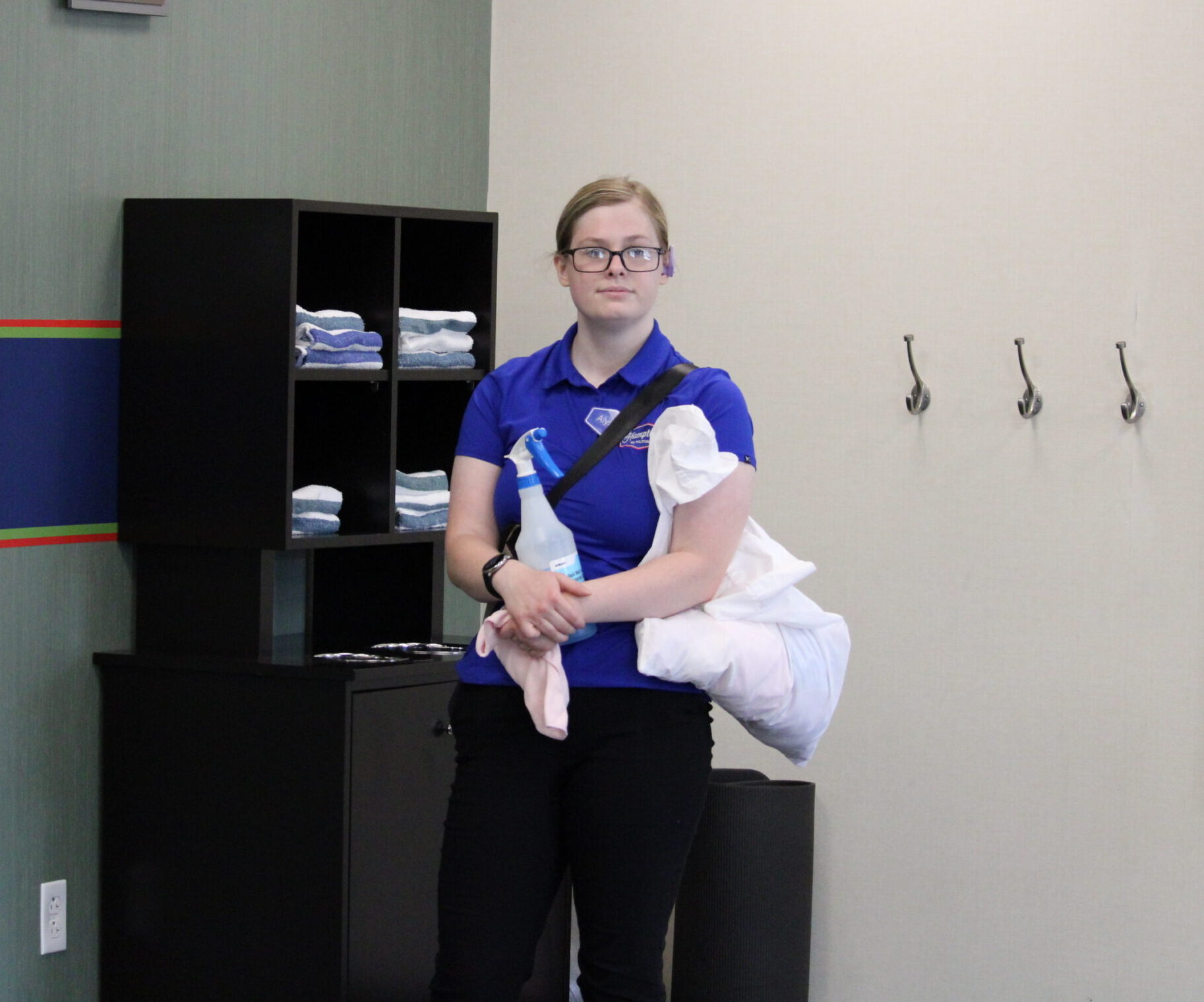Alyssa stands at work with a spray bottle and towel